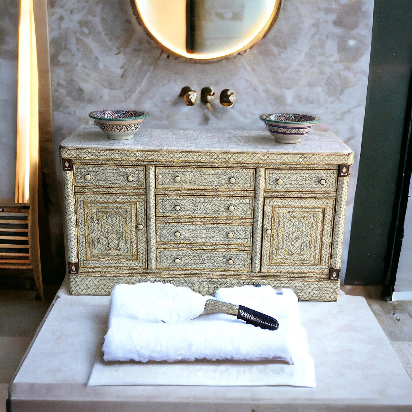 A white shell mother of pearl vanity sink cabinet with gold accents, featuring a marble top and multiple drawers, displayed in a bathroom setting with towels and a razor on top.
