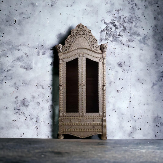 Antique wooden armoire with mother-of-pearl and bone inlay, with a marble top, against a textured wall.