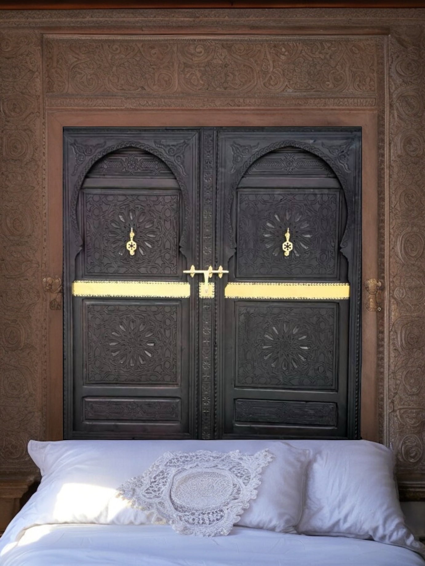 A vintage carved cedar double door headboard bed with brass knockers and intricate moorish artwork.