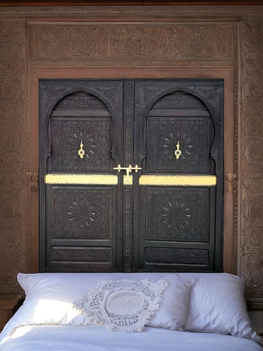 A vintage carved cedar double door headboard bed with brass knockers and intricate moorish artwork.