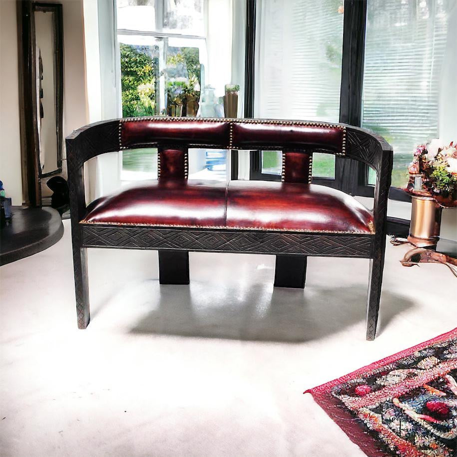 A luxurious Moroccan leather upholstered bench with hand carved cedar wood legs, placed in a well-lit room with a decorative rug on the floor and a window in the background.