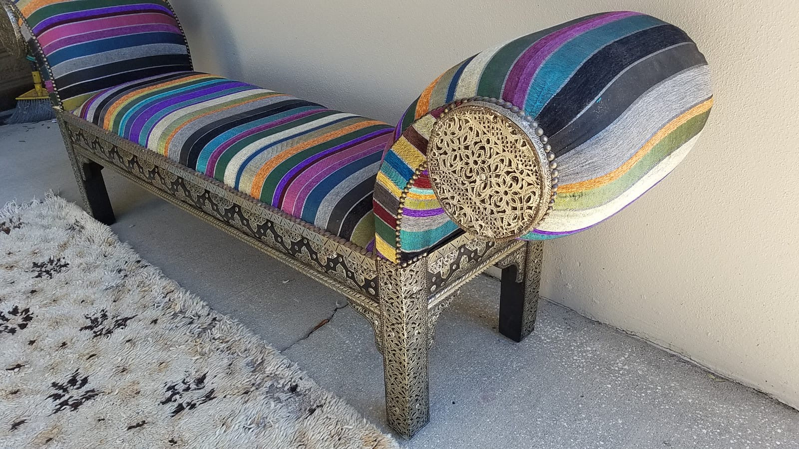 Colorful striped Moroccan lounge bench with intricate carvings on a light gray floor.