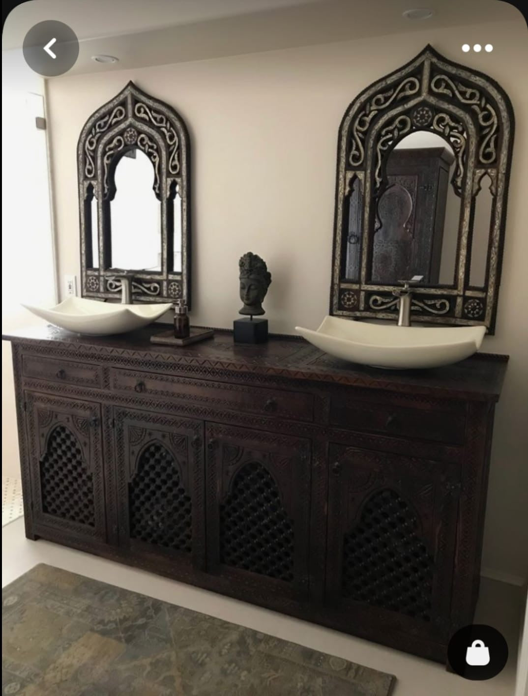 A carved wooden bathroom vanity with two sinks, mirrored by ornate mirrors with a dark mahogany stain finish.