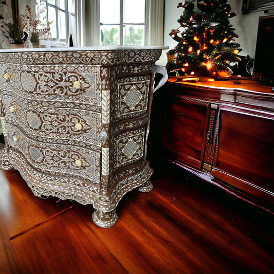 Antique style mother of pearl inlay cabinet with drawers, placed in a room with wooden flooring and a decorated Christmas tree in the background.